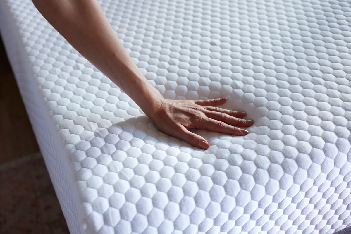 Hand pressing down on essential mattress