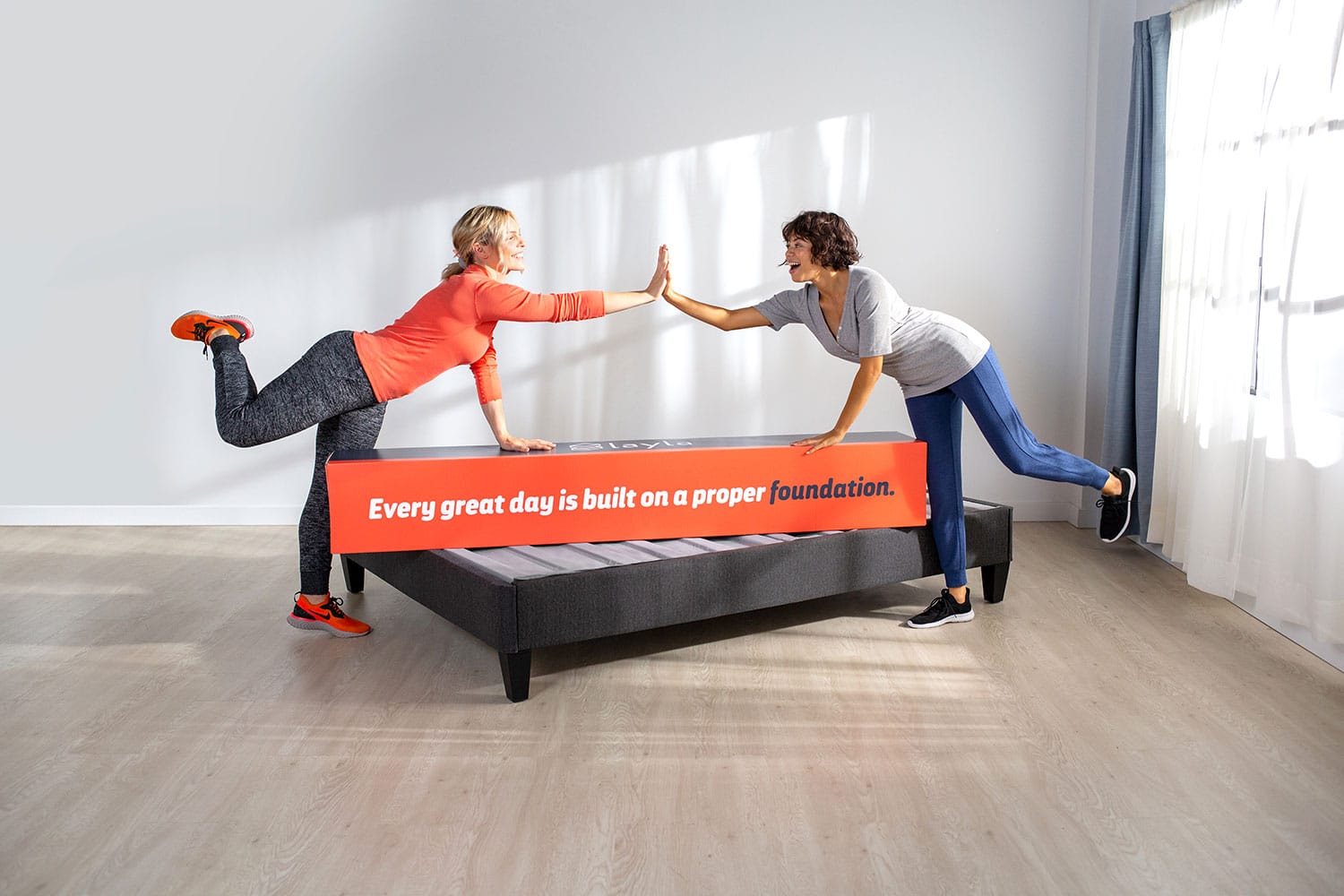 Two women high-fiving over a platform bed