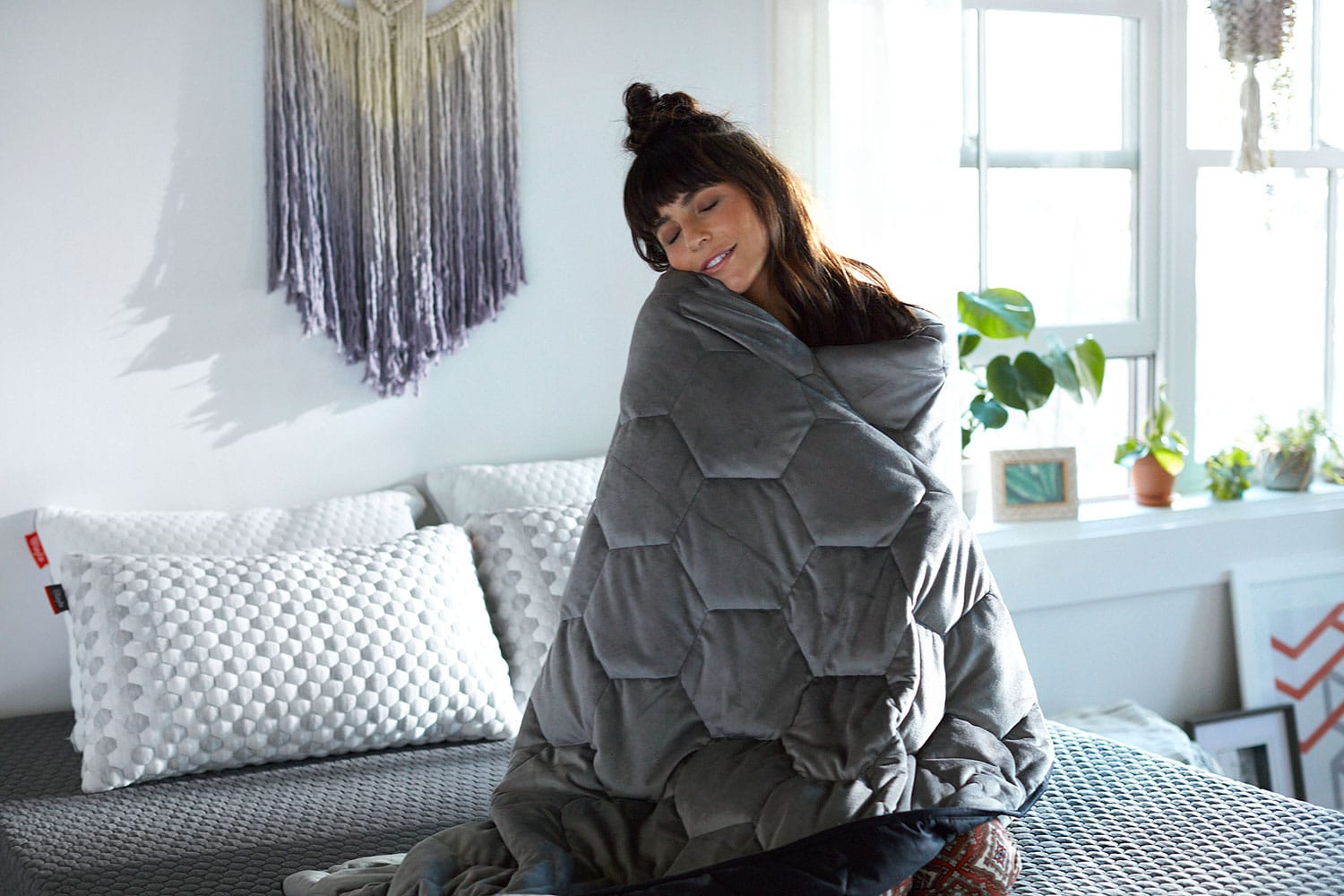 Woman kneeling on bed with a weighted blanket wrapped around her body