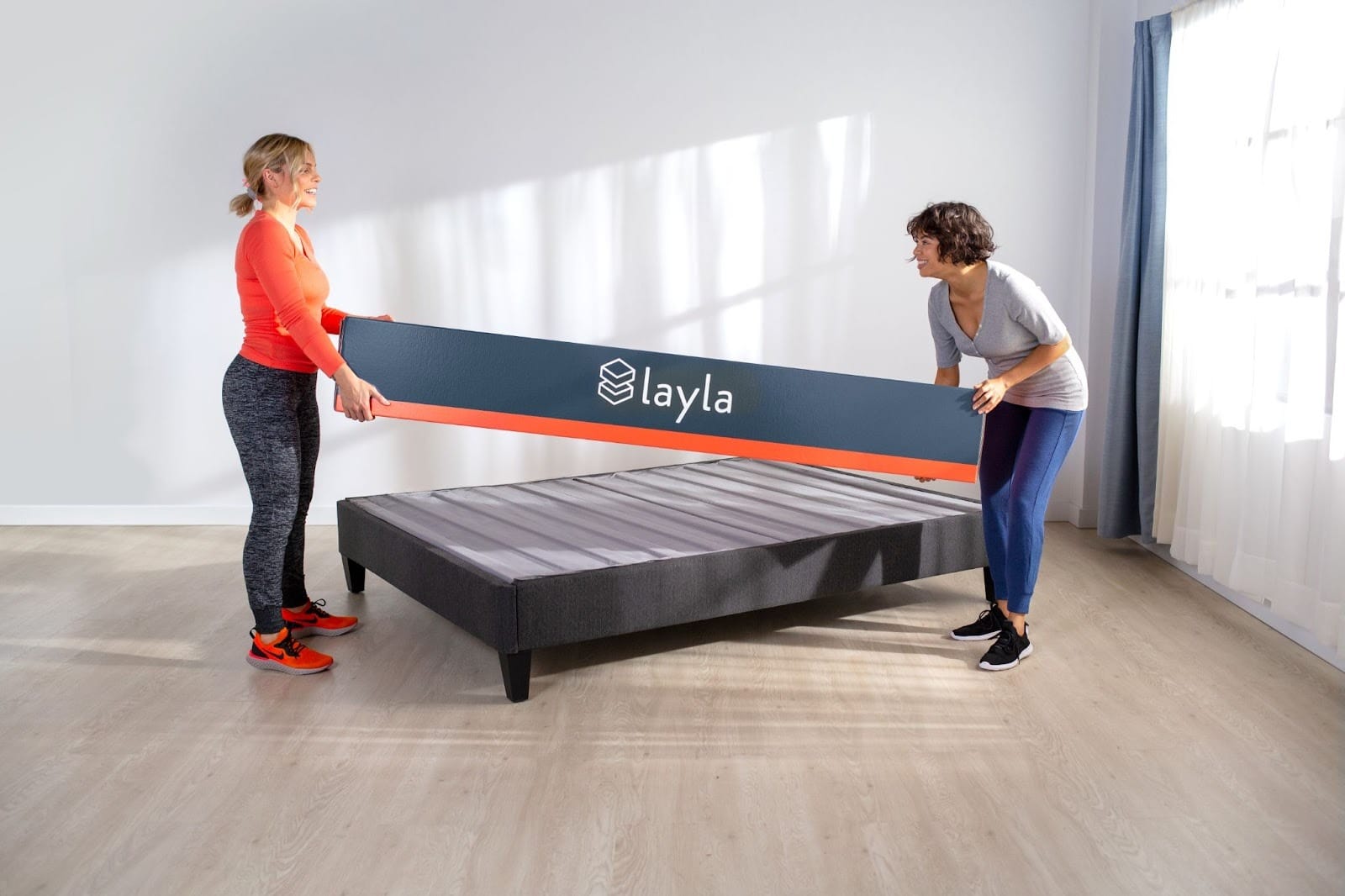 Two women carrying the Platform Bed box in a room with a Platform Bed
