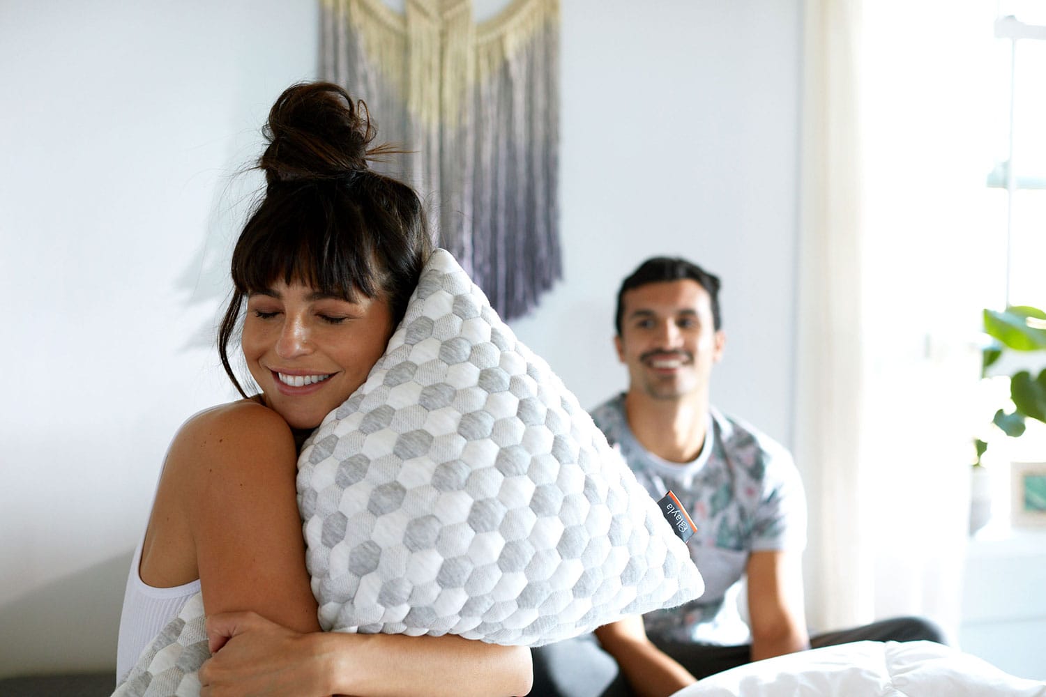 Man and woman sitting, with the woman hugging the Kapok Pillow