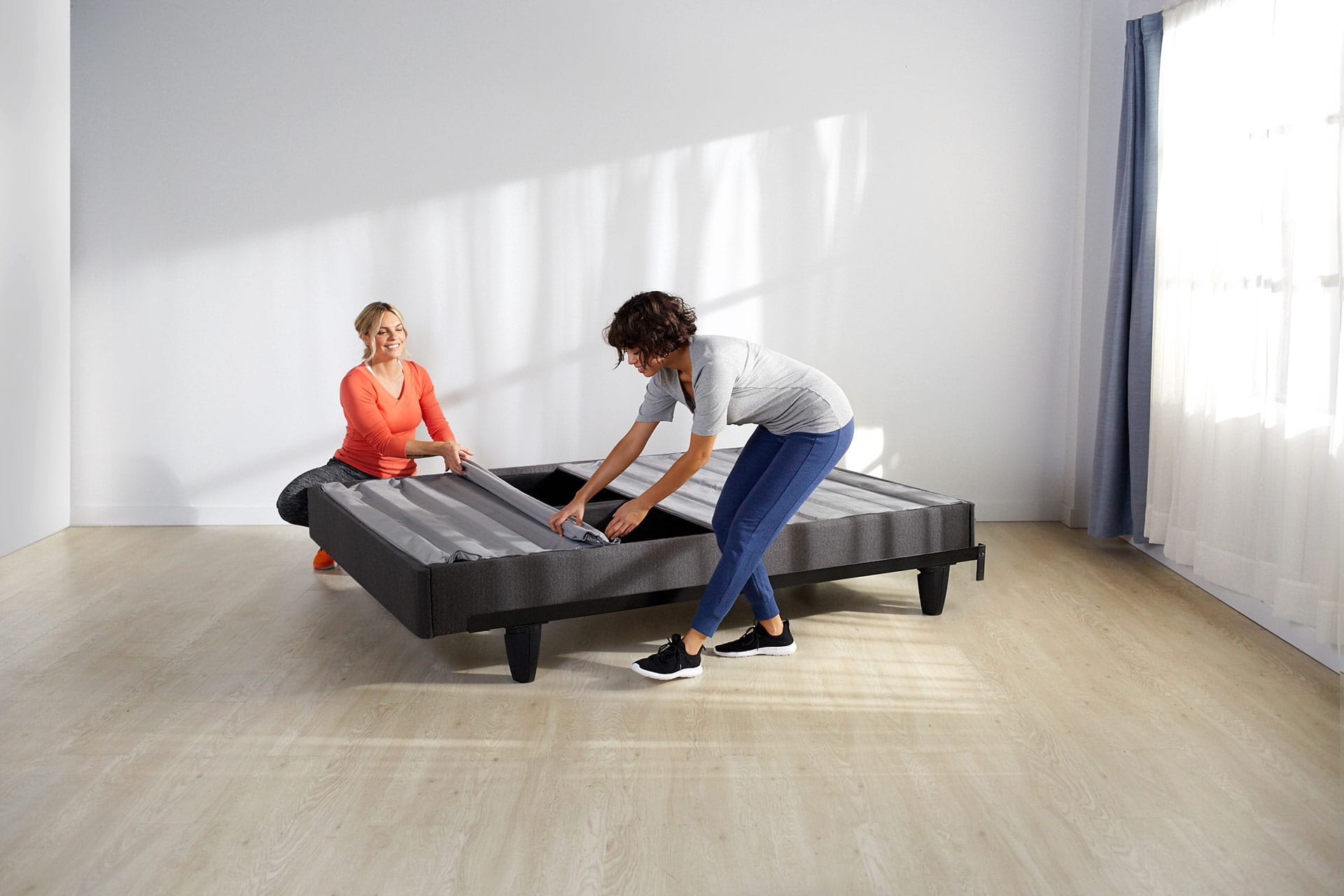 Two women rolling out the slat pack on the mattress foundation